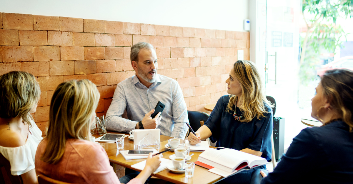 Five people sitting around a table talking business at a coffee shop. 